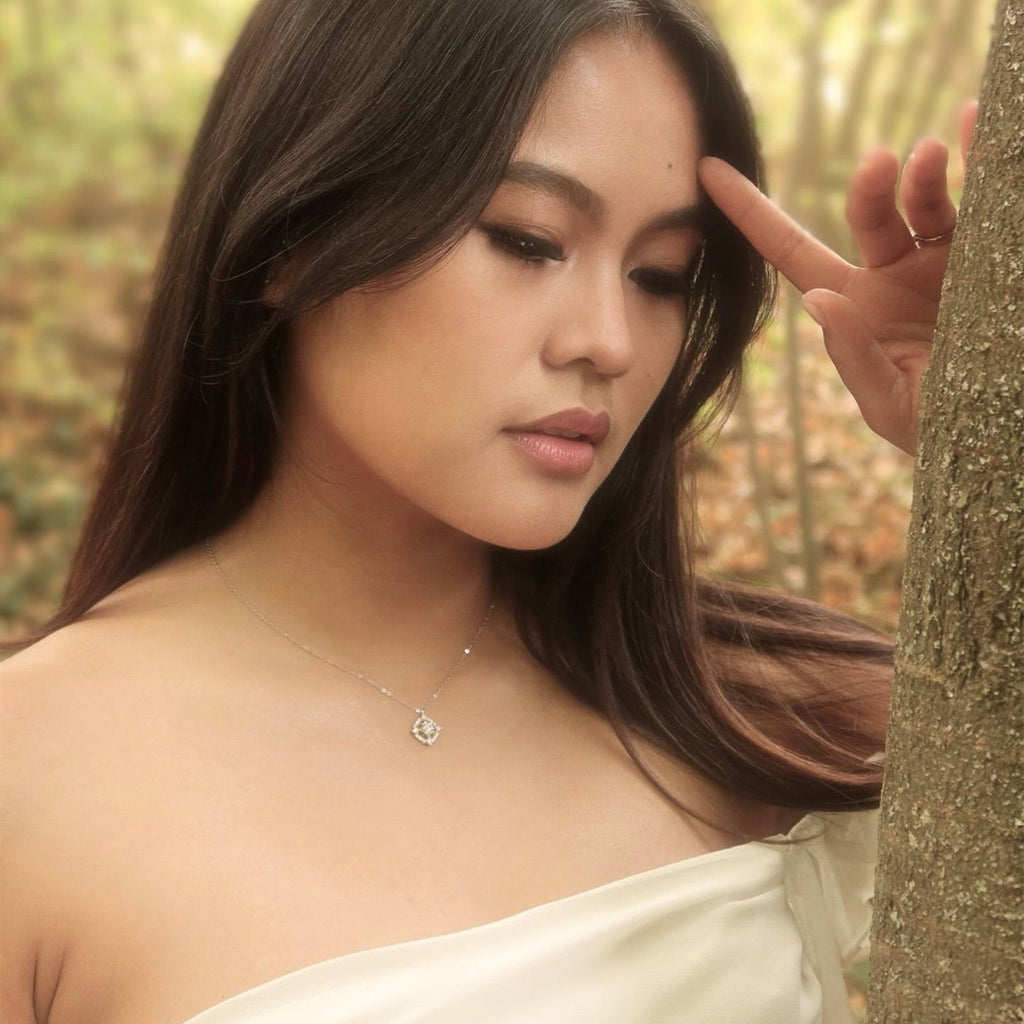 Sterling silver halo pendant necklace worn by a woman in an off-shoulder ivory dress, photographed in soft natural light in a forest setting. The square halo design sparkles against her skin, creating an elegant, ethereal look.