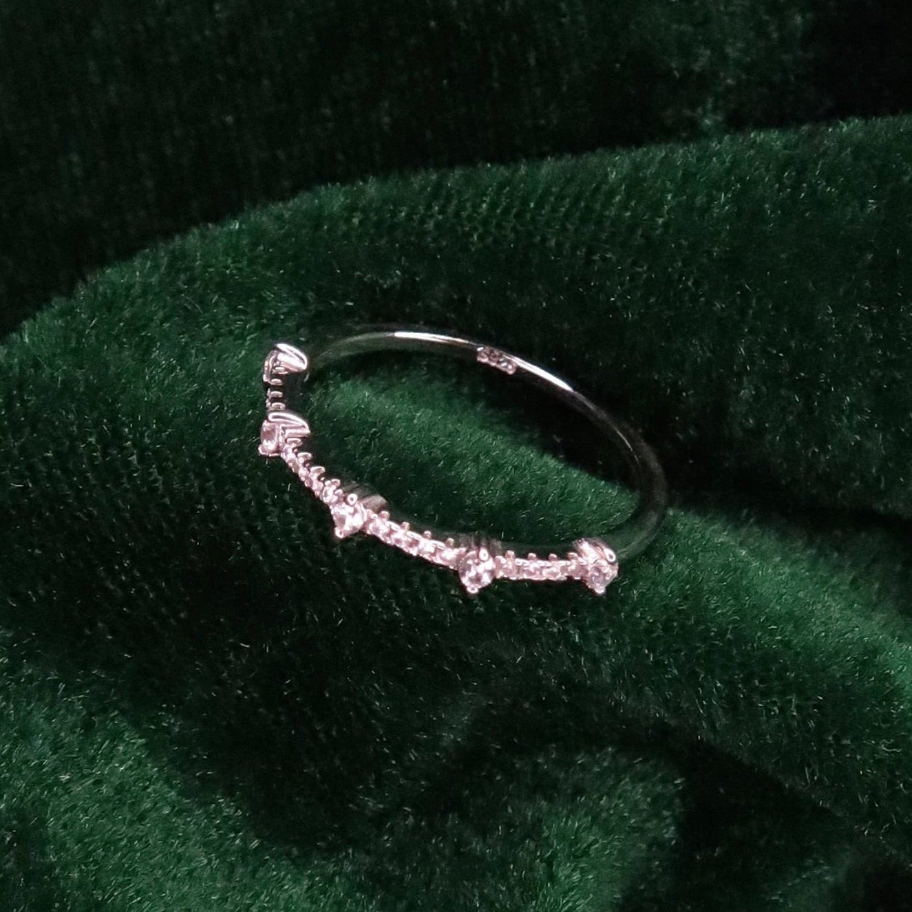 Delicate sterling silver band with small round stones spaced along the front, displayed on deep green velvet fabric for a refined, luxurious presentation.