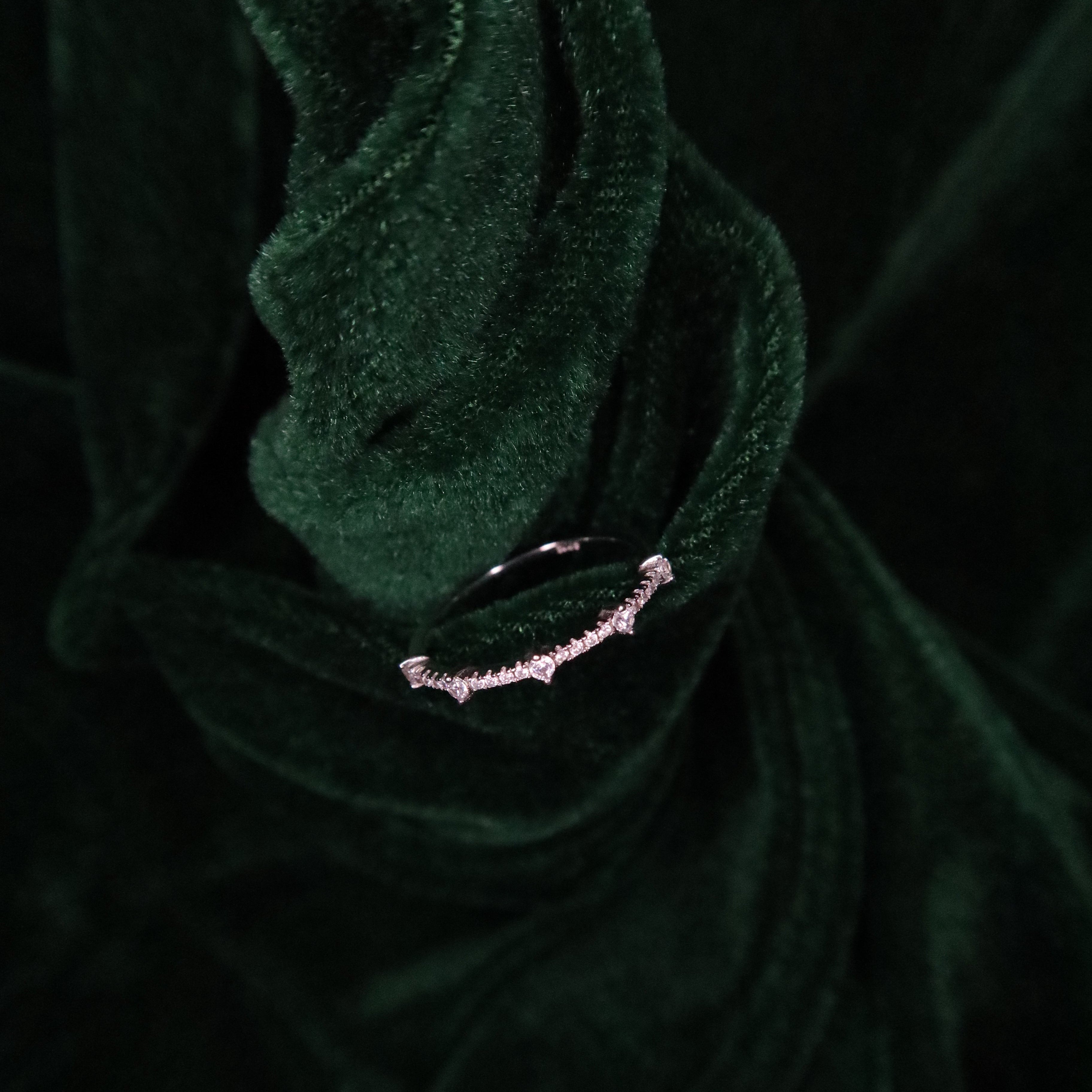 Delicate sterling silver band with small round stones arranged along the front, displayed on sculpted deep green velvet fabric for a refined, luxurious presentation.