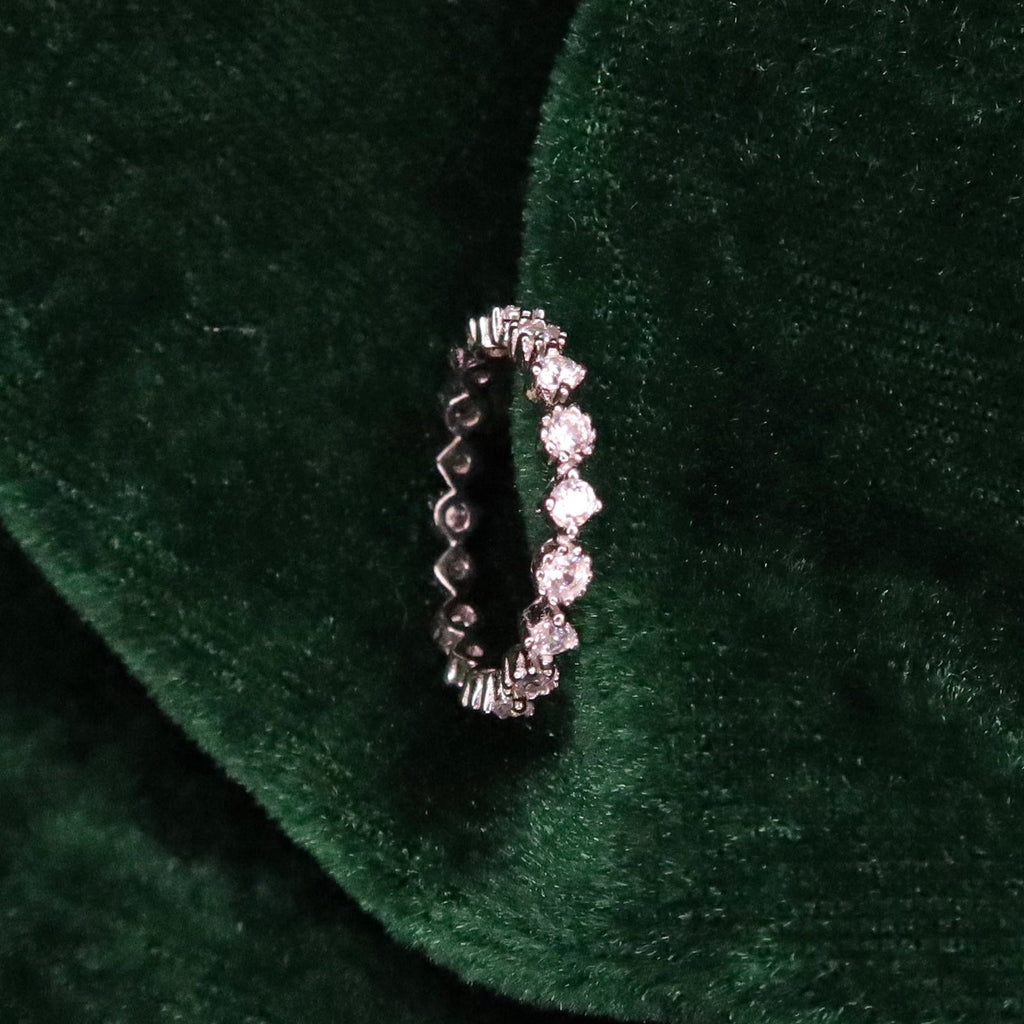 Sterling silver eternity ring with round sparkling stones set around the band, displayed upright on deep green velvet fabric for a luxurious presentation.