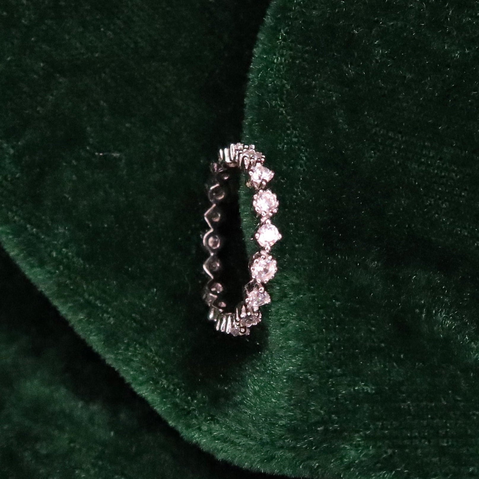 Sterling silver eternity ring with round sparkling stones set around the band, displayed upright on deep green velvet fabric for a luxurious presentation.