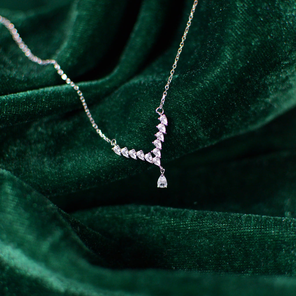 Close-up photograph of a sterling silver Y-shaped necklace resting on deep green velvet. The pear-cut cubic zirconia drop and graduated stones shimmer against the soft velvet folds, highlighting the necklace’s delicate, elegant design.