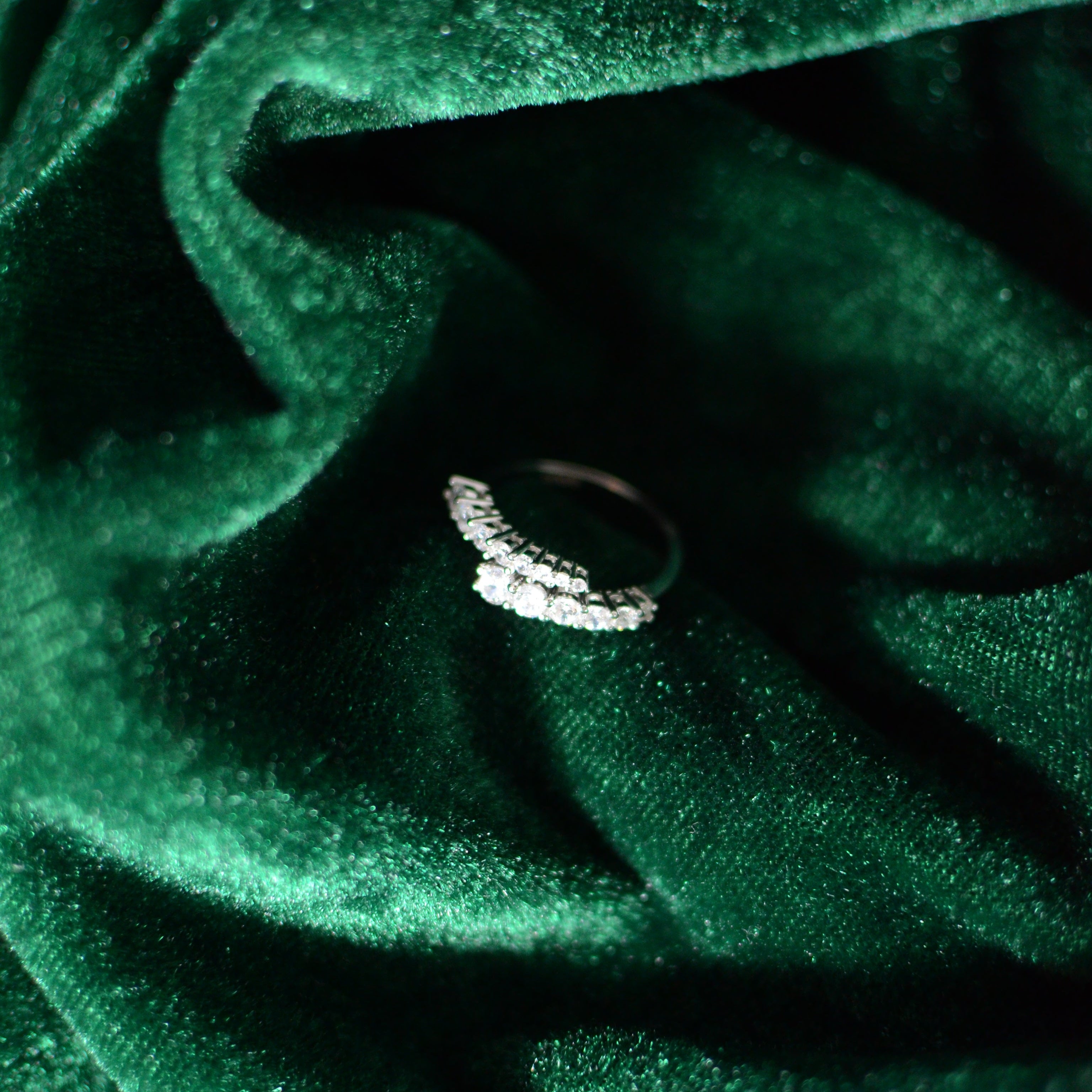 Sterling silver ring with graduated round stones displayed on deep green velvet fabric, captured with soft lighting for an elegant, luxurious presentation.