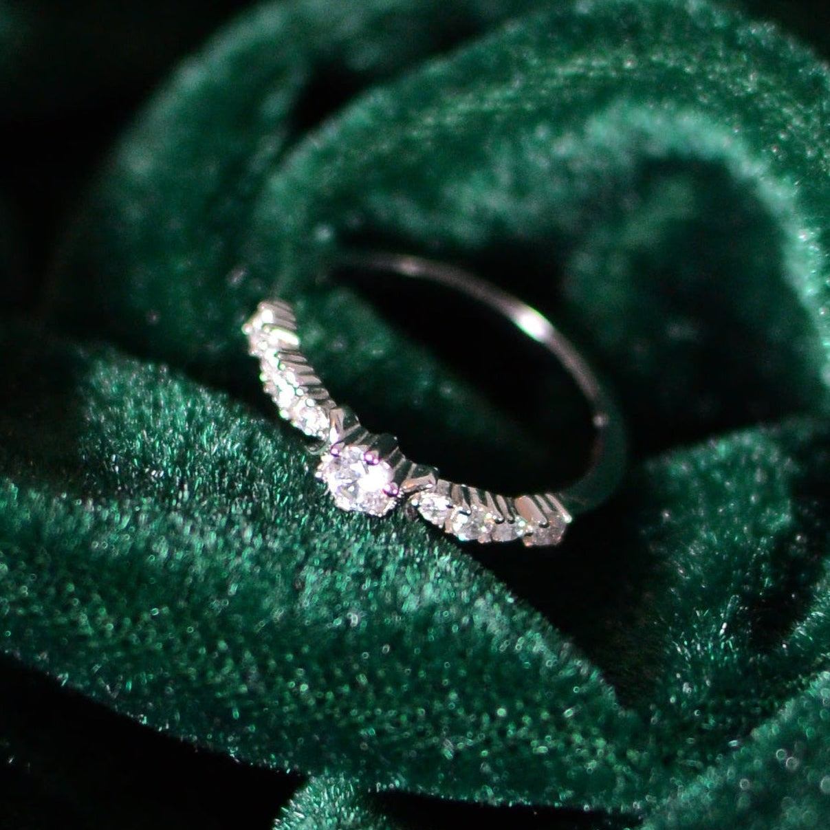 Sterling silver ring with a round center stone and tapered baguette-style accents, displayed on deep green velvet fabric for an elegant, refined presentation.