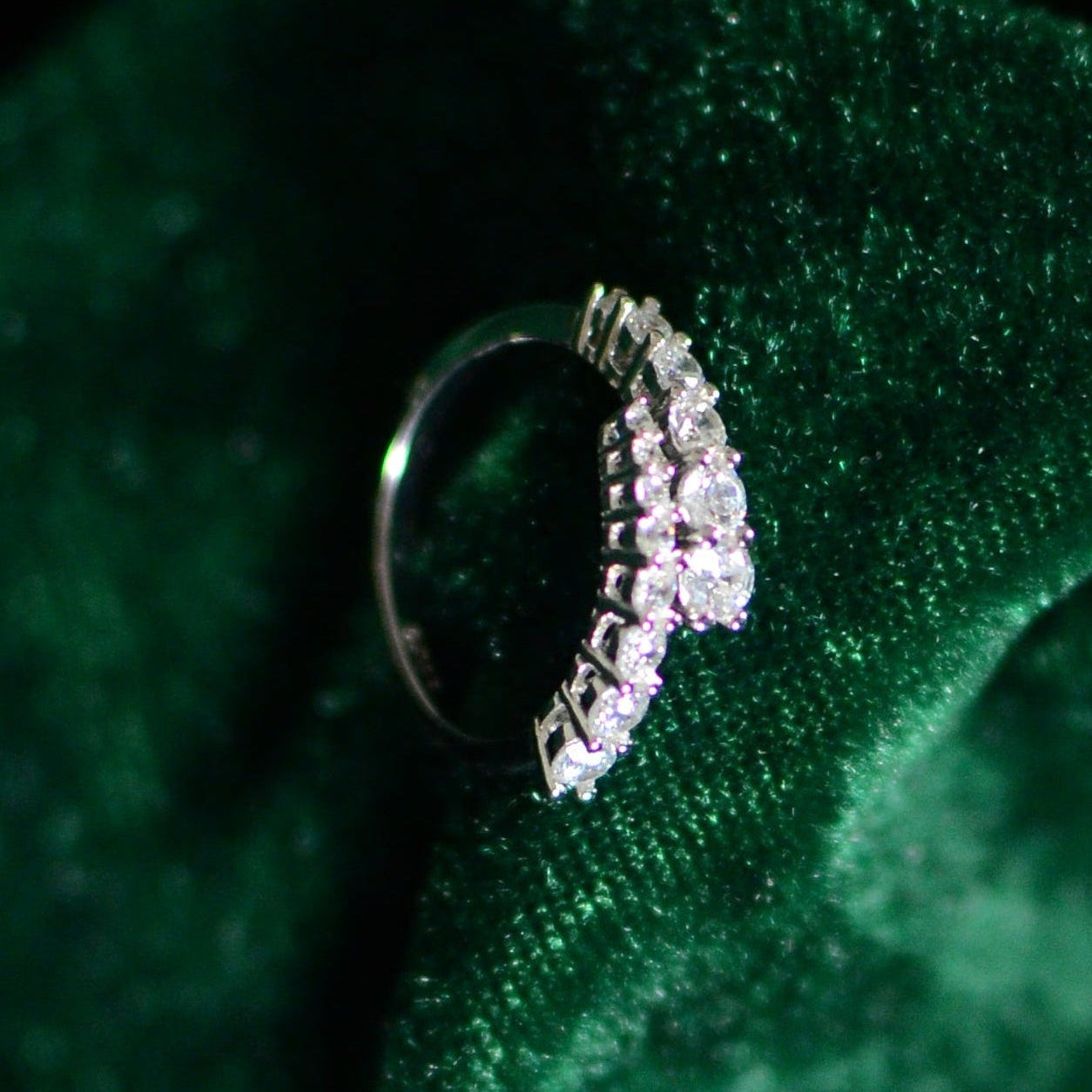 Sterling silver ring with clustered round stones arranged in a graduated pattern, displayed on deep green velvet fabric for a luxurious, high-contrast presentation.