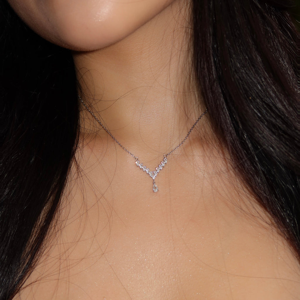 Close-up portrait of a woman wearing a sterling silver Y-shaped necklace with a pear-cut cubic zirconia drop. The pendant rests on her collarbone, catching the light against her smooth, glowing skin and dark hair.