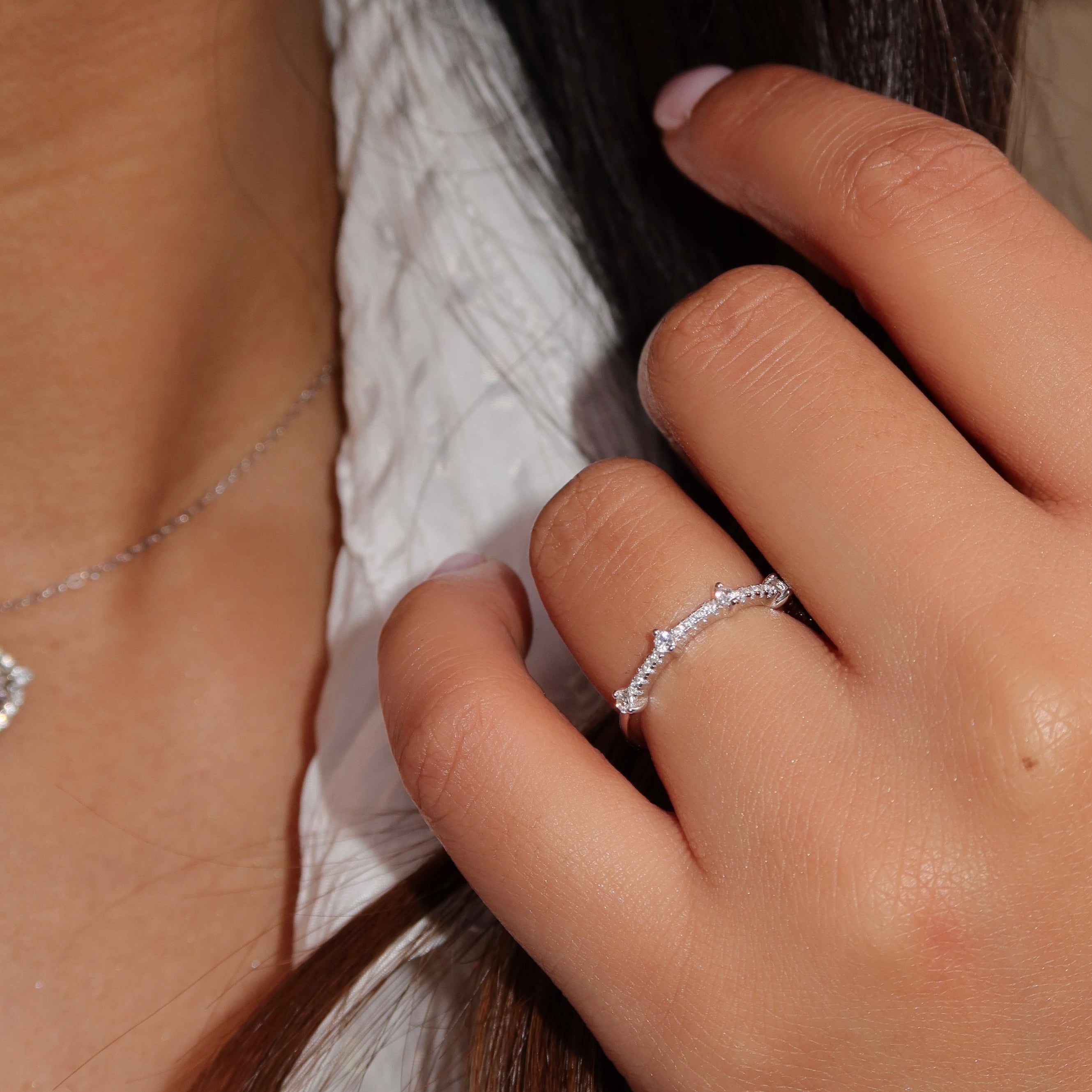 Close-up of a woman wearing a delicate sterling silver band with small round stones, her hand gently touching her hair while dressed in a white textured top.