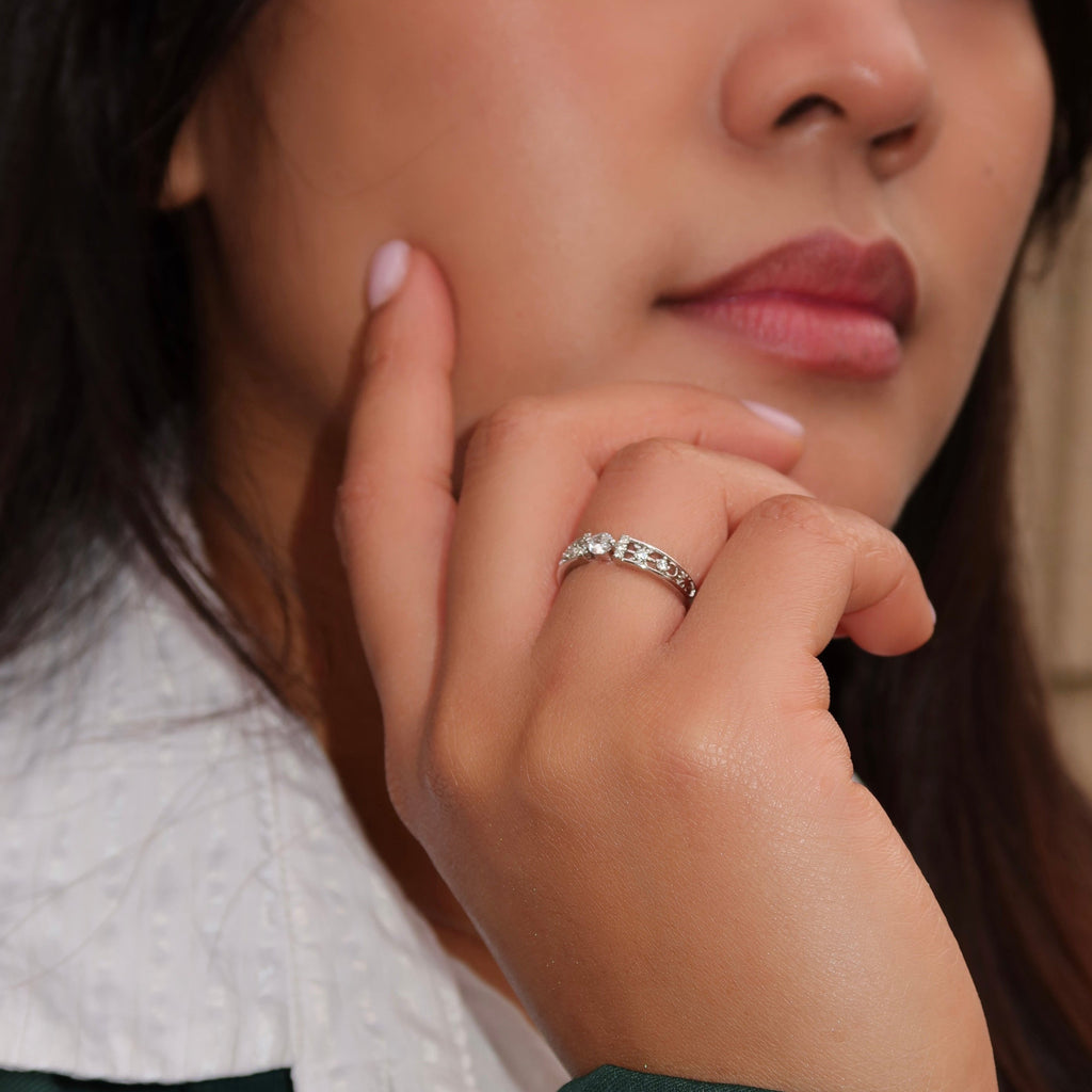 Close-up of a woman wearing a sterling silver ring with a round center stone and detailed side accents, her hand resting near her face while dressed in a green top with a white textured collar.