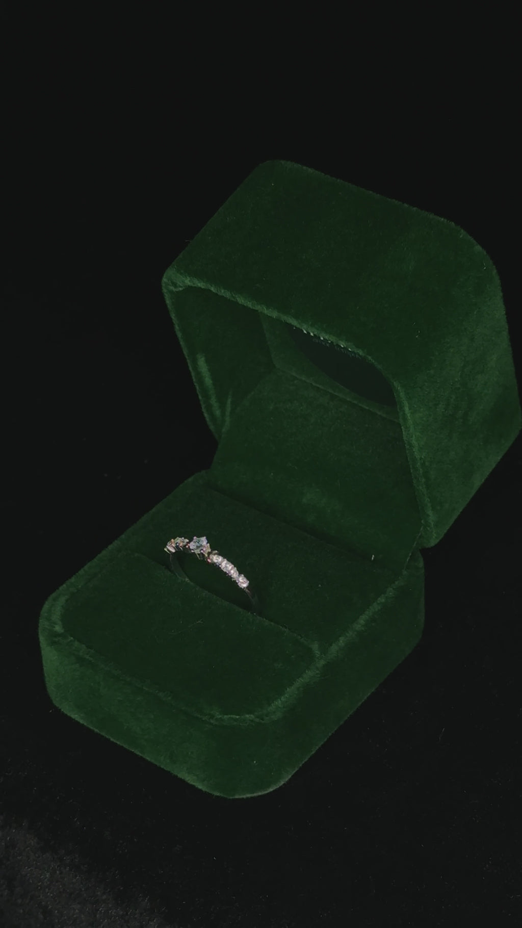 Video of a sterling silver eternity ring rotating inside a green velvet jewelry box, highlighting the sparkle of its round stones as it catches the light from different angles.