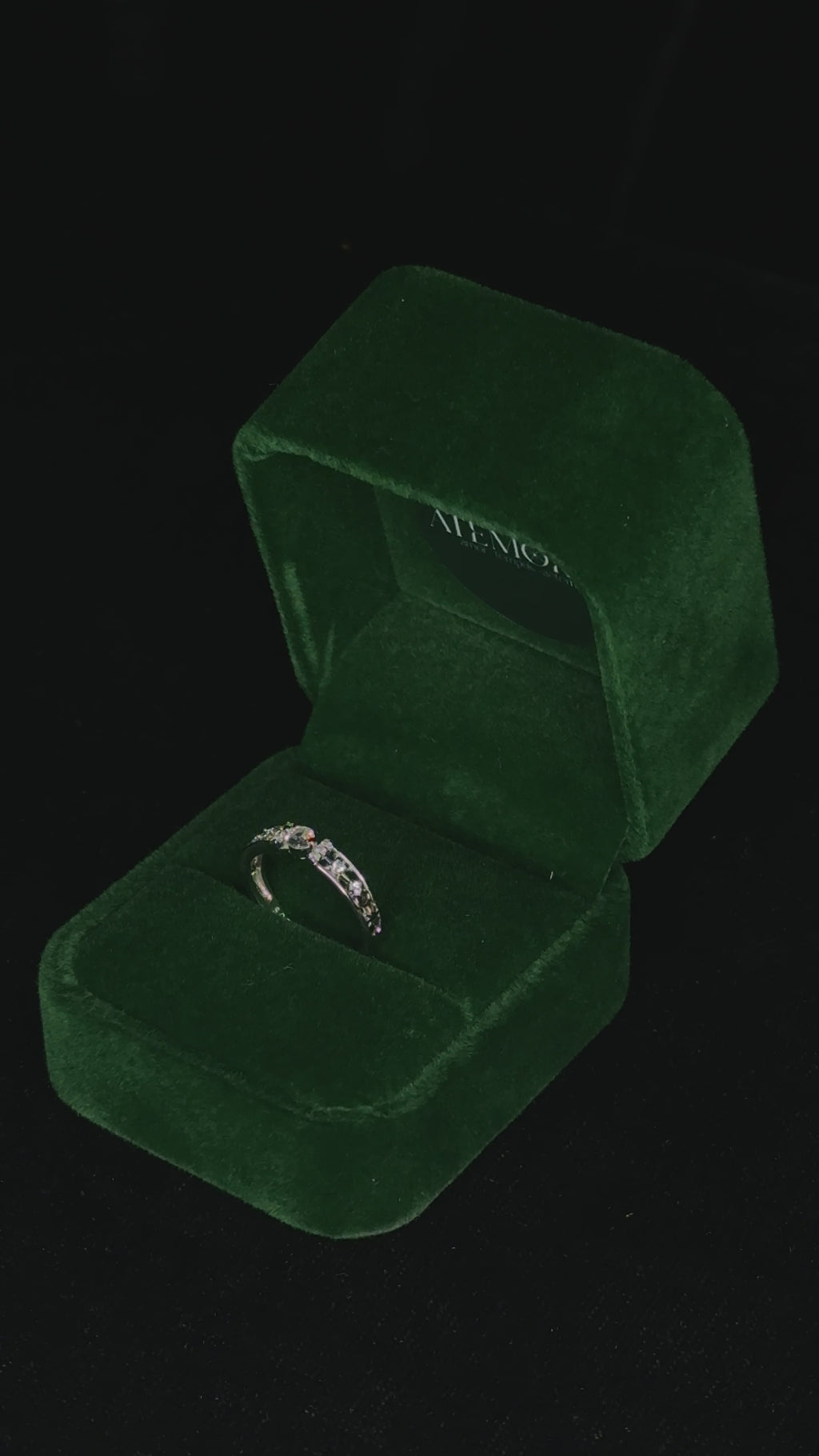 Video of a sterling silver ring with a round center stone and detailed side accents rotating inside a green velvet jewelry box, catching the light to reveal its sparkle and craftsmanship.
