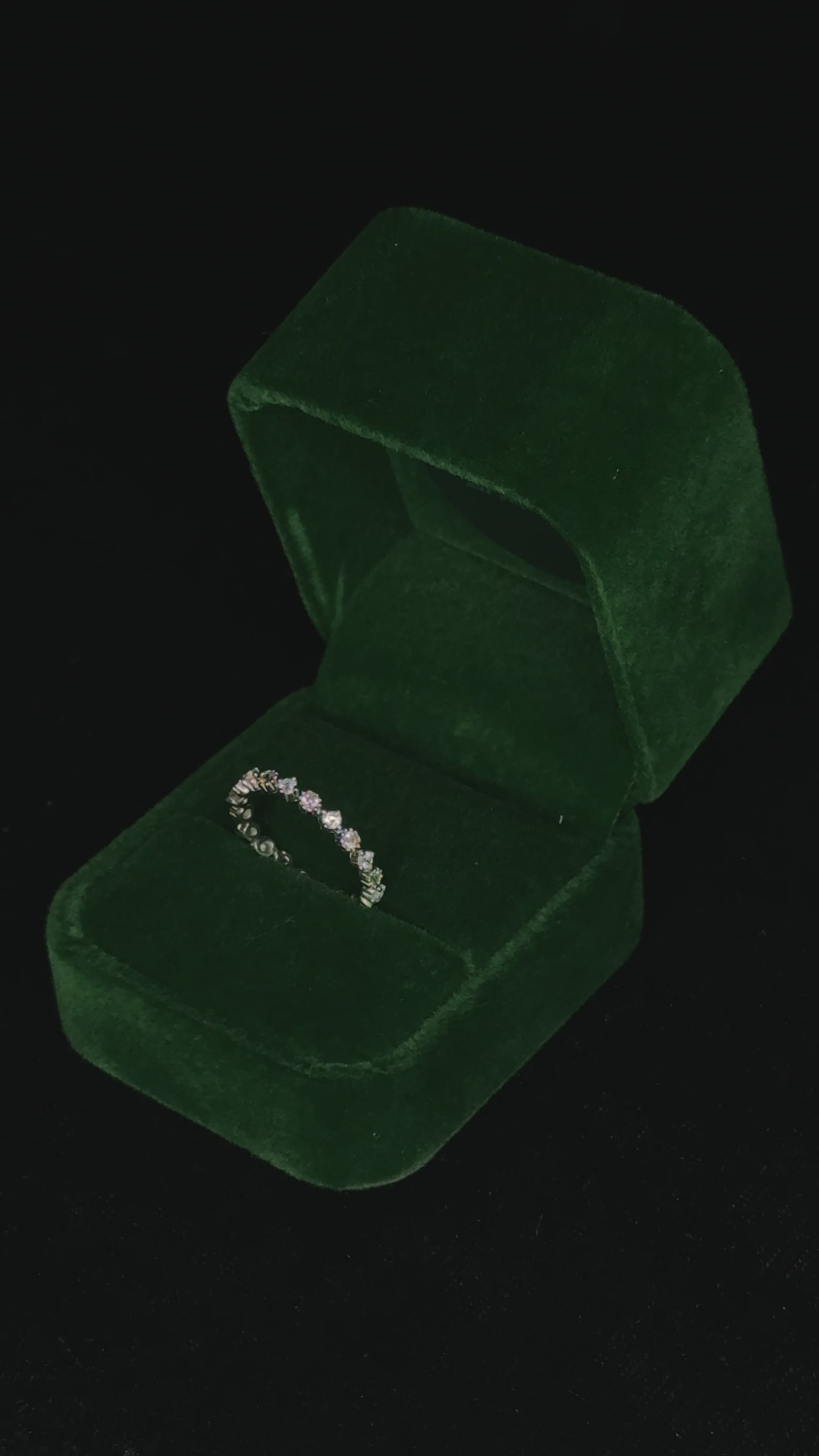Video of a sterling silver eternity ring rotating inside a green velvet jewelry box, catching the light to highlight the sparkle of its round stones and detailed band.