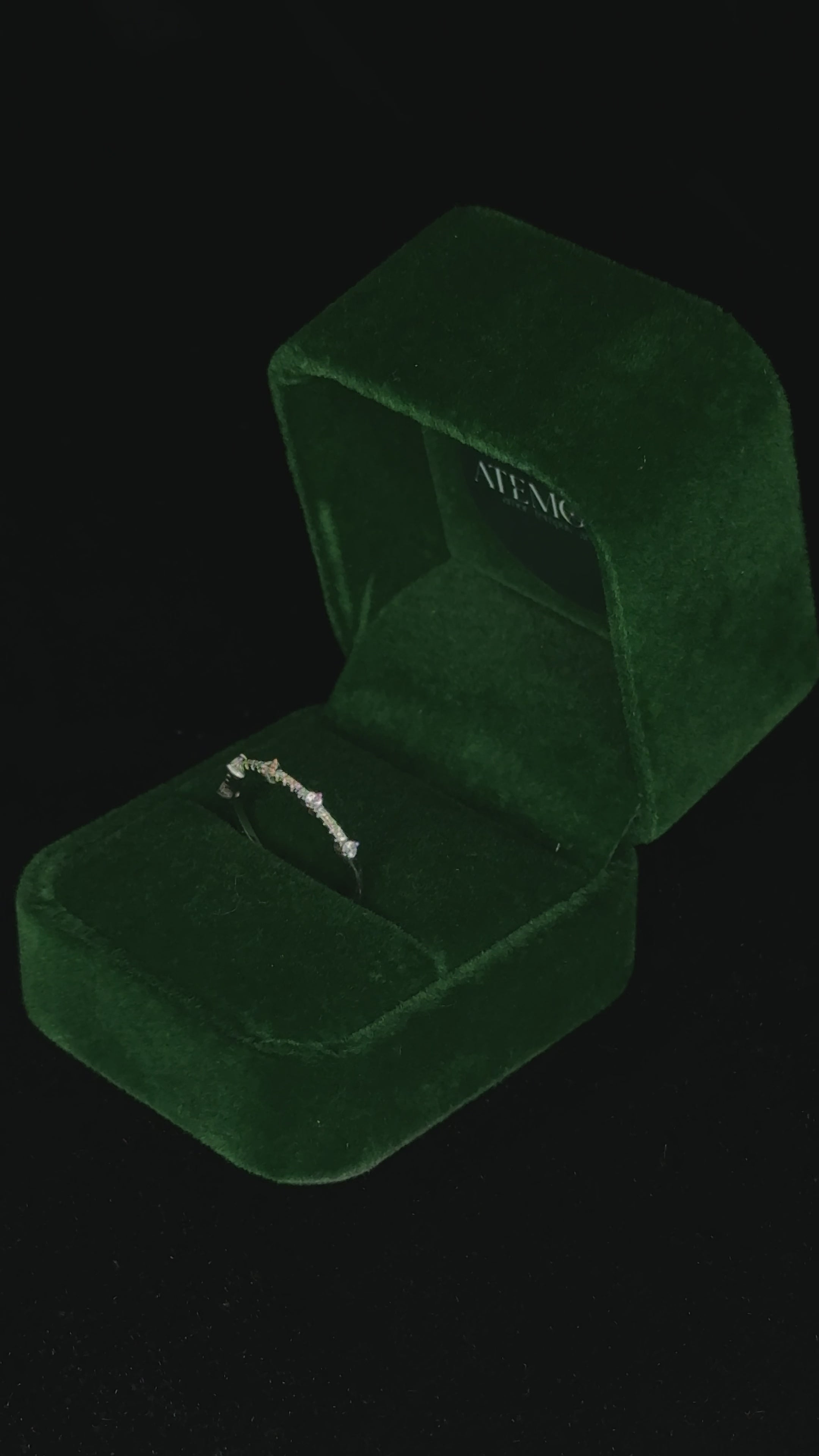 Video of a delicate sterling silver band with small round stones rotating inside a green velvet jewelry box, catching the light to highlight its sparkle and fine detailing.