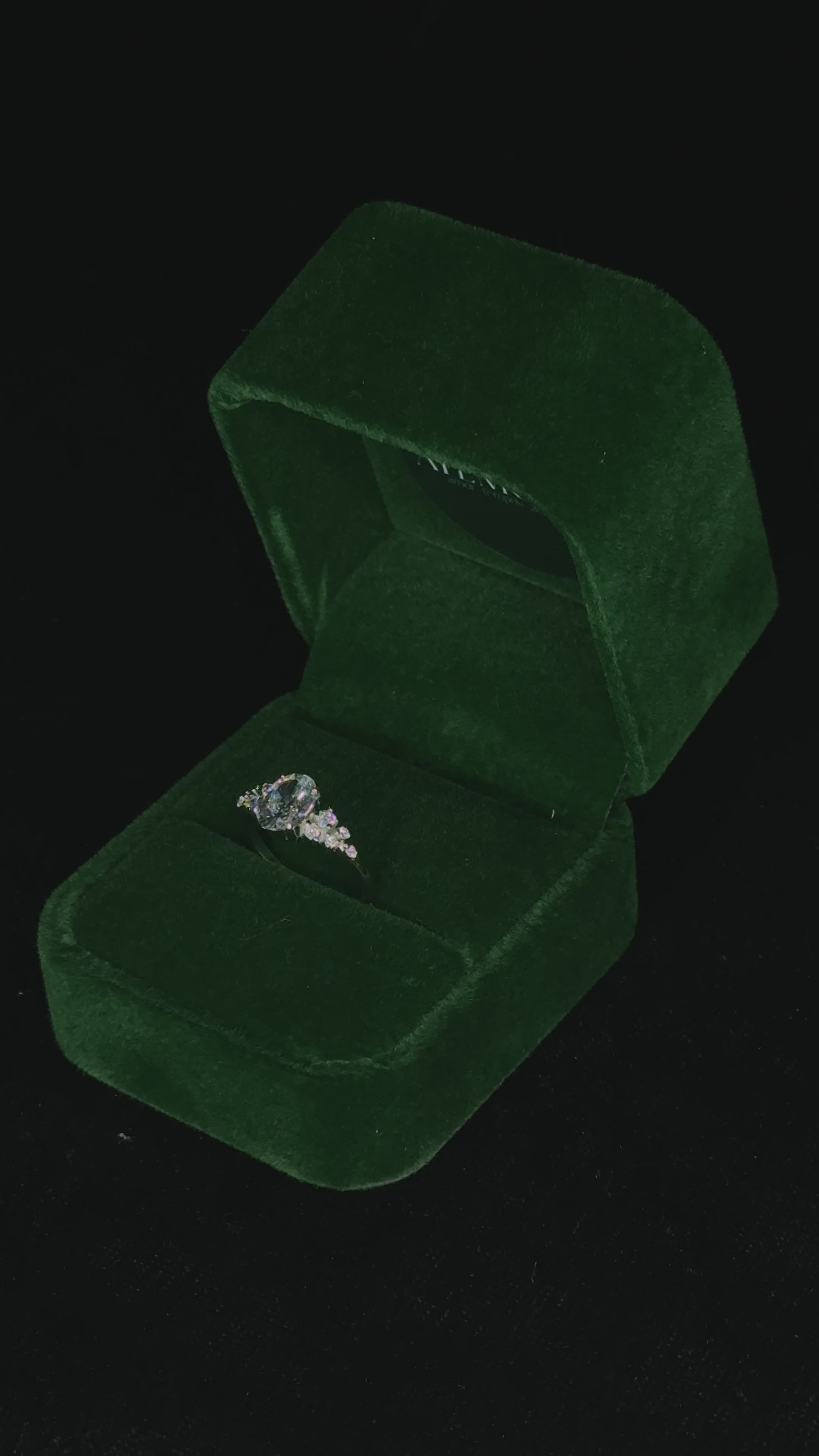Video of a sterling silver ring with an oval-cut center stone and tapered side stones rotating inside a green velvet jewelry box, catching the light to show its sparkle and details.