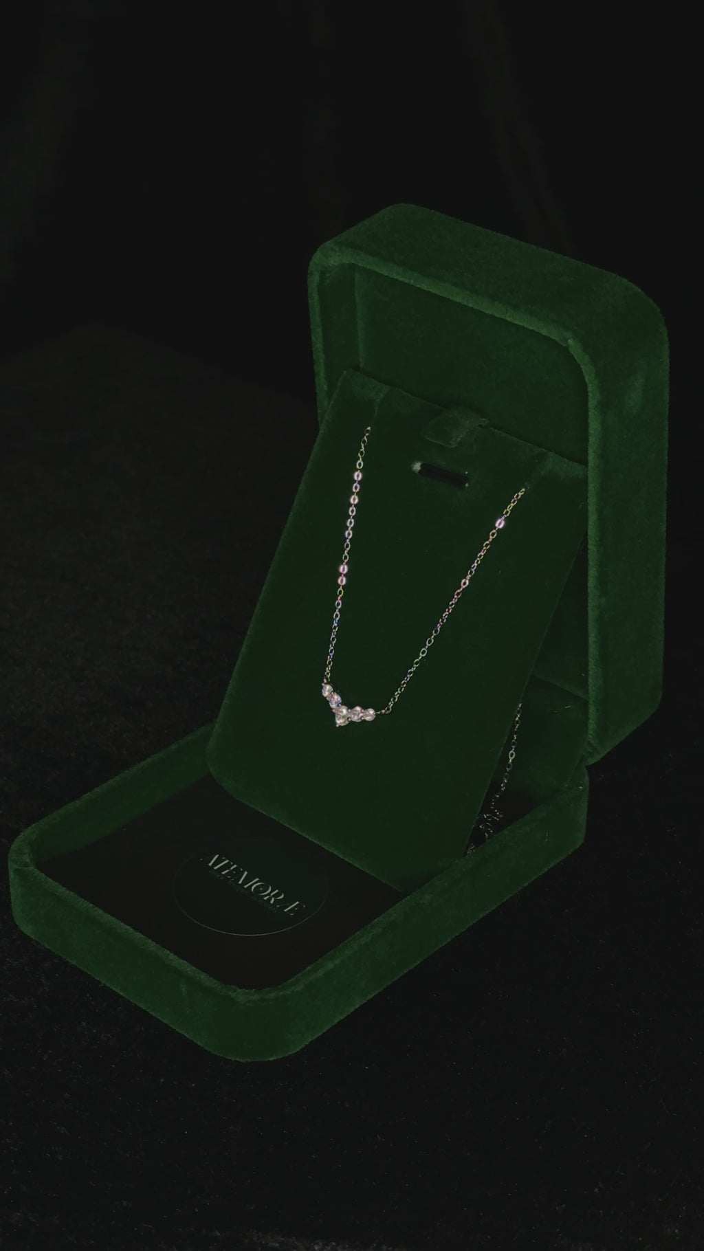 Close-up video of a sterling silver V-shaped cubic zirconia necklace slowly rotating inside a deep green velvet jewelry box. The pendant catches the light as it turns, showing the brilliance of the clustered stones against the rich velvet backdrop.