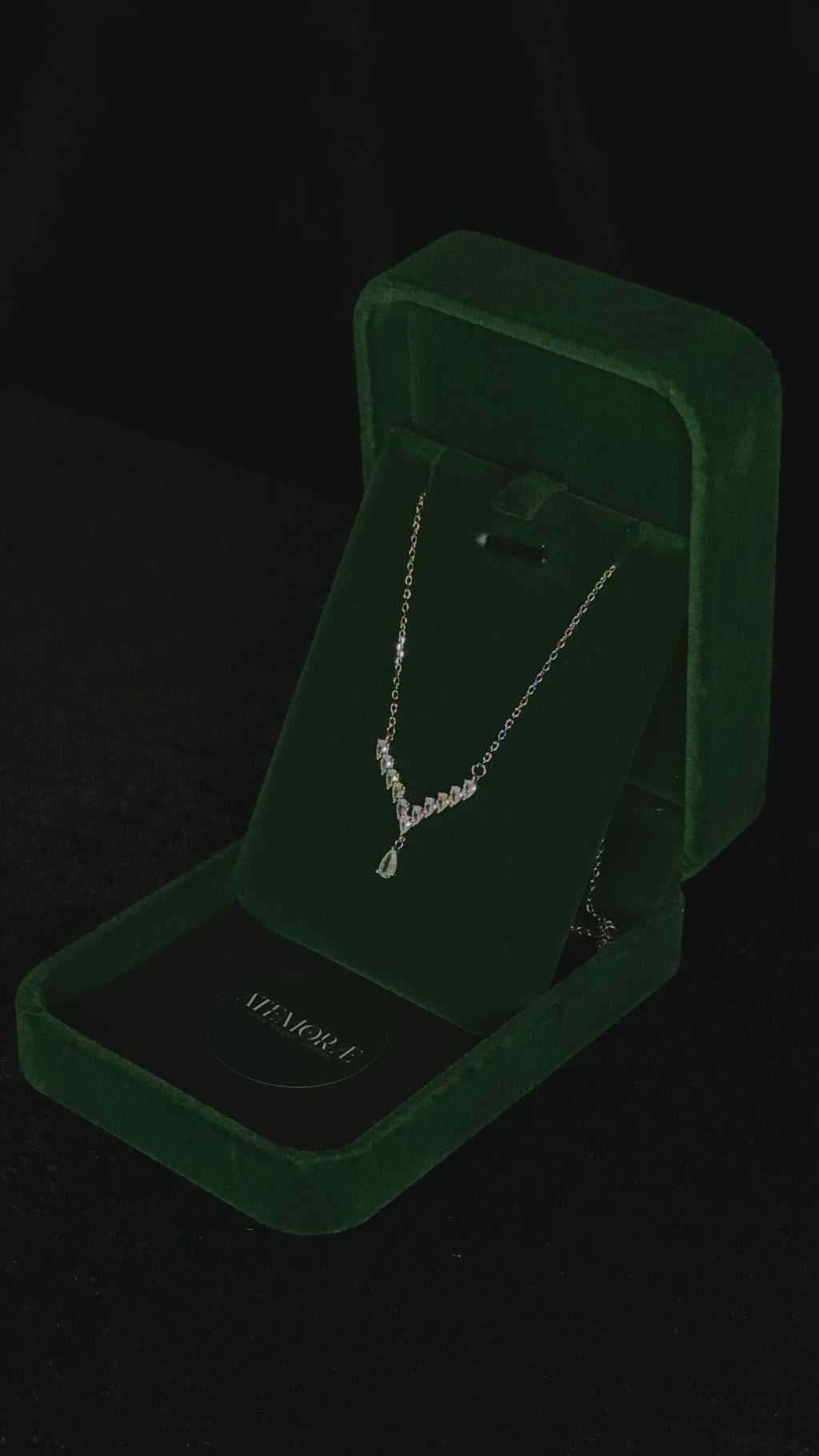 Close-up video of a sterling silver Y-shaped necklace rotating inside a deep green velvet jewelry box. The graduated cubic zirconia stones and pear-cut drop catch the light as the pendant turns, creating a shimmering, elegant sparkle against the velvet backdrop.