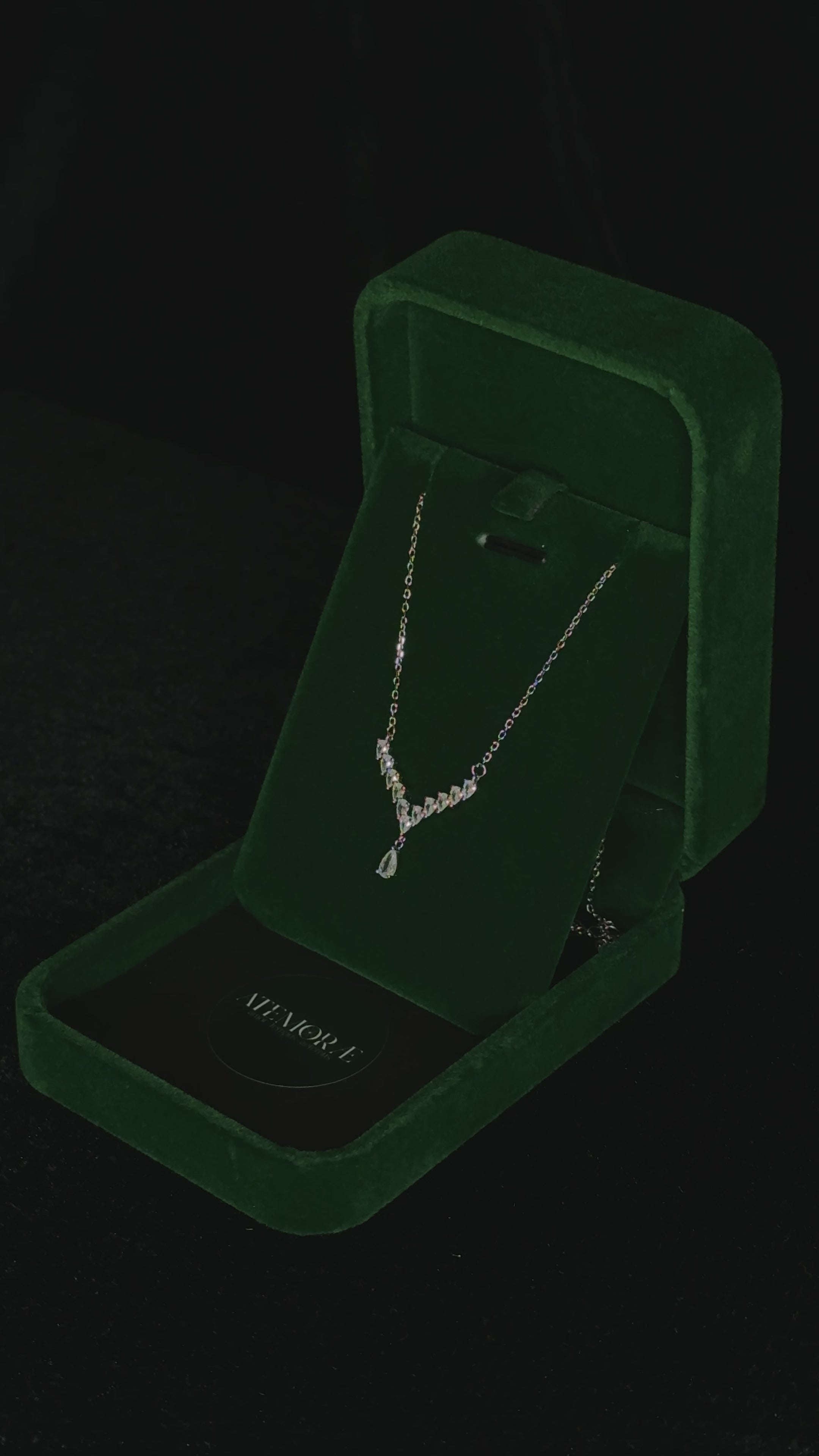 Close-up video of a sterling silver Y-shaped necklace rotating inside a deep green velvet jewelry box. The graduated cubic zirconia stones and pear-cut drop catch the light as the pendant turns, creating a shimmering, elegant sparkle against the velvet backdrop.